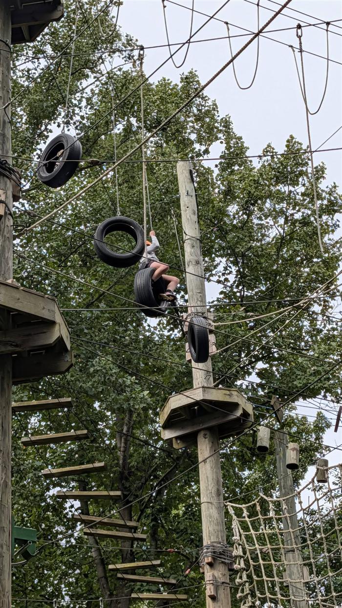 A Troop 58 Scout mid-air on the tire traverse element of the high ropes challenge course
